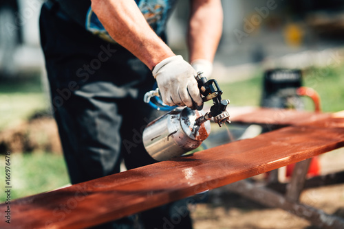 Close-up details of man using spray gun or airbrush for painting  fence. Carpentry details with woodwork and handyman photo