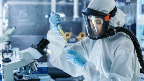 Medical Virology Research Scientist Works in a Hazmat Suit with Mask, She Uses Micropipette. She Works in a Sterile High Tech Laboratory, Research Facility.