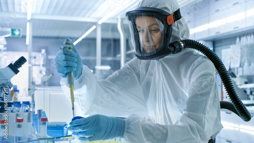 Obraz na płótnie Medical Virology Research Scientist Works in a Hazmat Suit with Mask, She Uses Micropipette