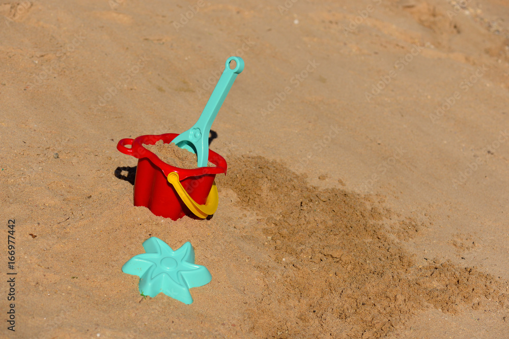 Baby beach toys - bucket, shovel and pask in the sand on a sunny day. Baby beach toys - bucket, shovel and pask in the sand on a sunny day.