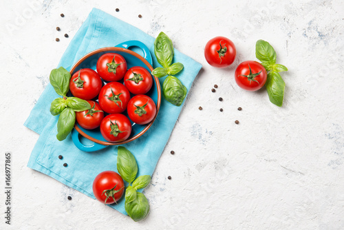 Fresh cherry tomatoes in a bowl  basil leaves and black pepper on stone table  closeup  top view with copy space