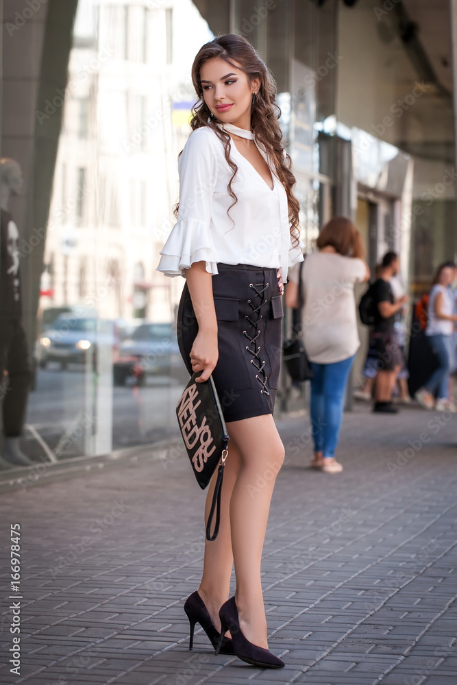 Portrait of a beautiful young girl outdoors in the city, standing in clothes