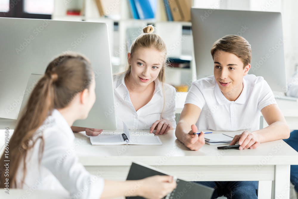 teenagers in white shirts having conversation during lesson in classroom teenagers in white shirts having conversation during lesson in classroom