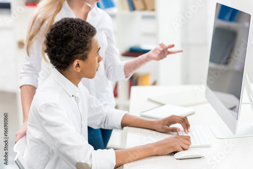 multicultural students discussing task at computer screen in class