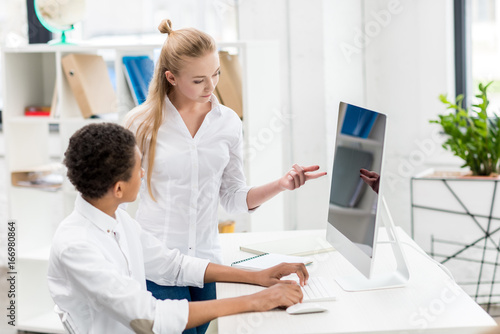 multicultural students discussing task at computer screen in class