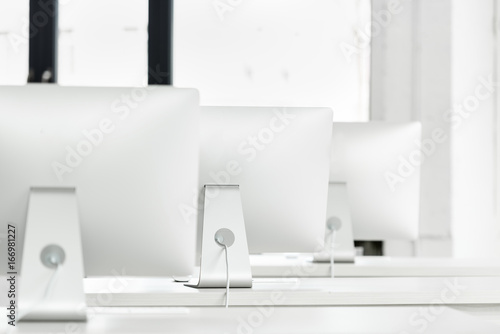 close up view of white computer monitors standing on tables in computer class