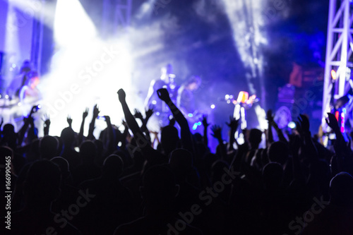 Blurred. Rear view of crowd with arms outstretched. cheering crowd at rock concert. silhouettes of concert crowd in front of bright stage lights. Crowd at music concert, audience raising hands up
