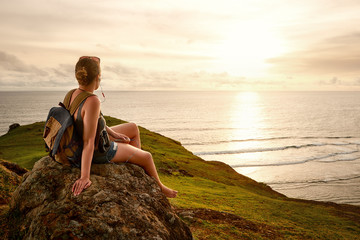 Hiker with backpack enjoying sunset listening to music on peak of mountain.
