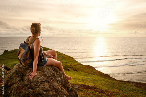 Hiker with backpack enjoying sunset listening to music on peak of mountain. photo