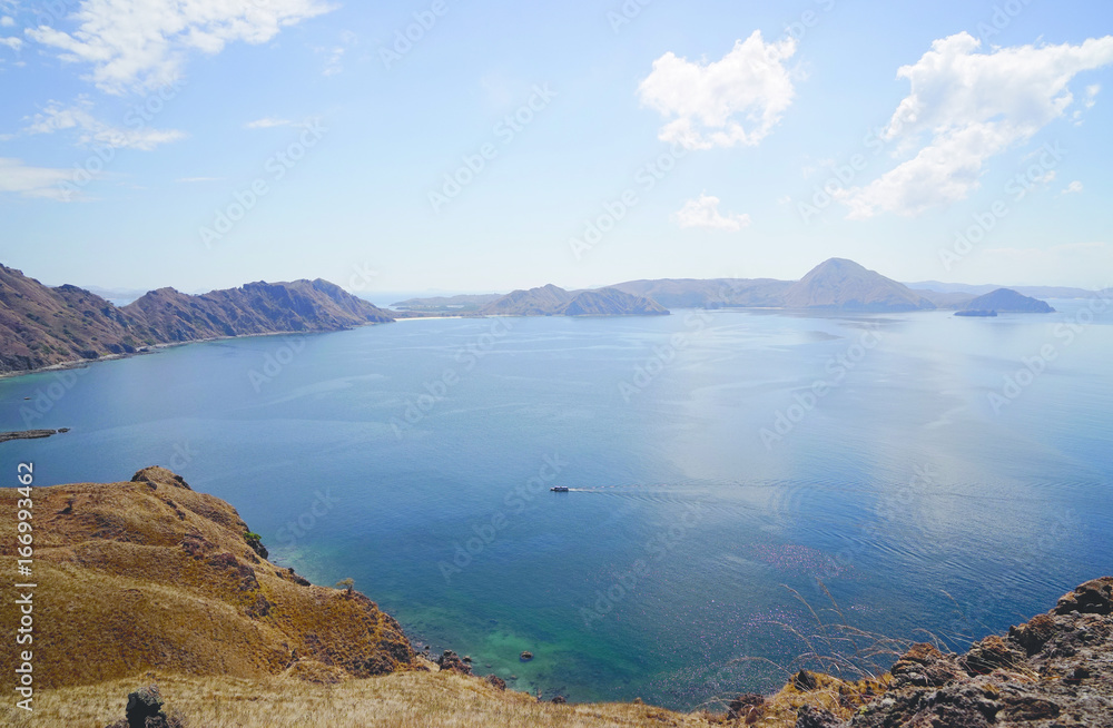 Panoramic blue sky view of the hills, mountains and ocean with a small boat from Padar Island part of komodo national park, Flores Indonesia.