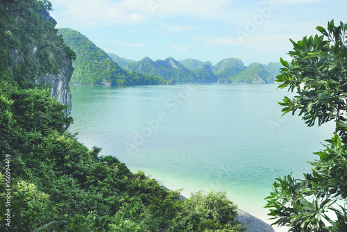 View of green islands in Halong Bay at day from a distance with empty white sand beach and turquoise water, UNESCO World Heritage Site, Vietnam, Southeast Asia.