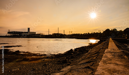 sun above the bay with some industrial buildings in the background © brian