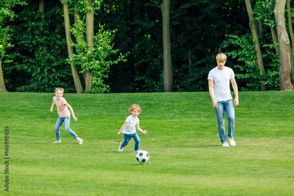 happy young father with two adorable children playing soccer on green lawn at park happy young father with two adorable children playing soccer on green lawn at park
