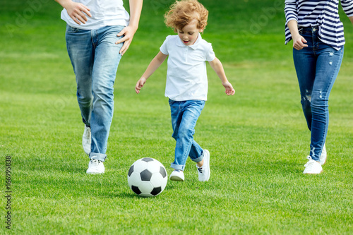 cropped shot of young parents with son playing soccer on green lawn
