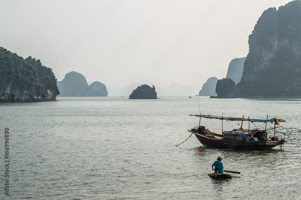 Limestone Formations, Fisherman and Boat in the Ocean at Ha Long Bay, Vietnam Limestone Formations, Fisherman and Boat in the Ocean at Ha Long Bay, Vietnam