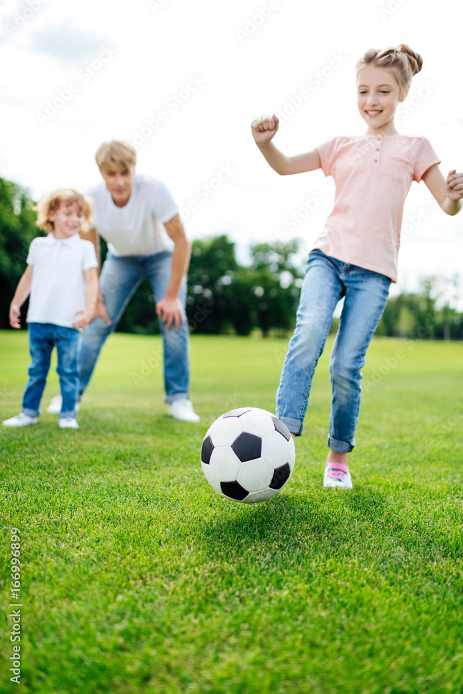 father with son looking at cute little girl kicking soccer ball on meadow father with son looking at cute little girl kicking soccer ball on meadow