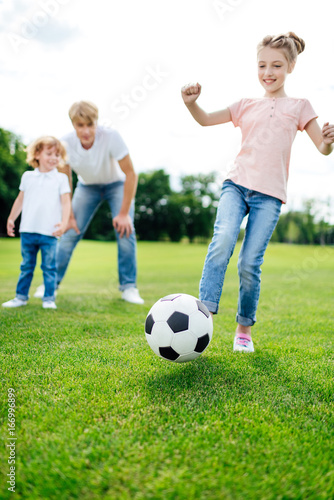 father with son looking at cute little girl kicking soccer ball on meadow © LIGHTFIELD STUDIOS
