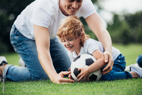 happy father and son playing with soccer ball on green grass at park