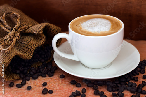 Coffee in a white cup and coffee beans on the table.