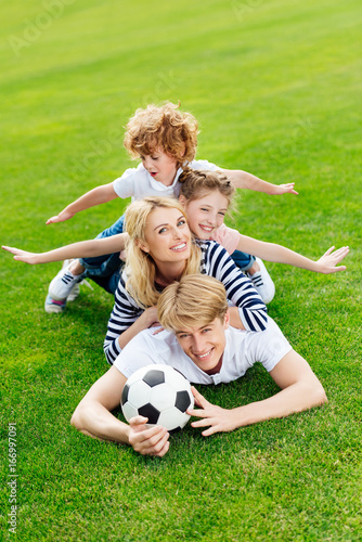 happy young family with soccer ball lying on green lawn at park