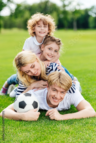 happy young family with soccer ball lying on green lawn at park