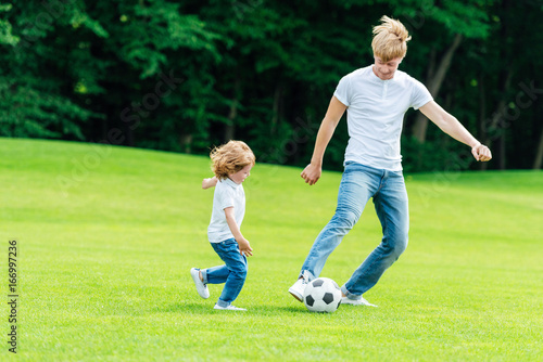 happy father and son playing soccer on green grass in park