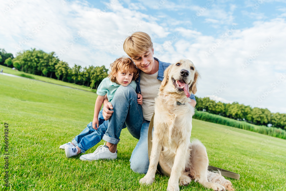 happy father and son looking at golden retriever dog at park happy father and son looking at golden retriever dog at park