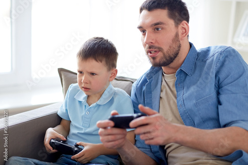 father and son playing video game at home © Syda Productions