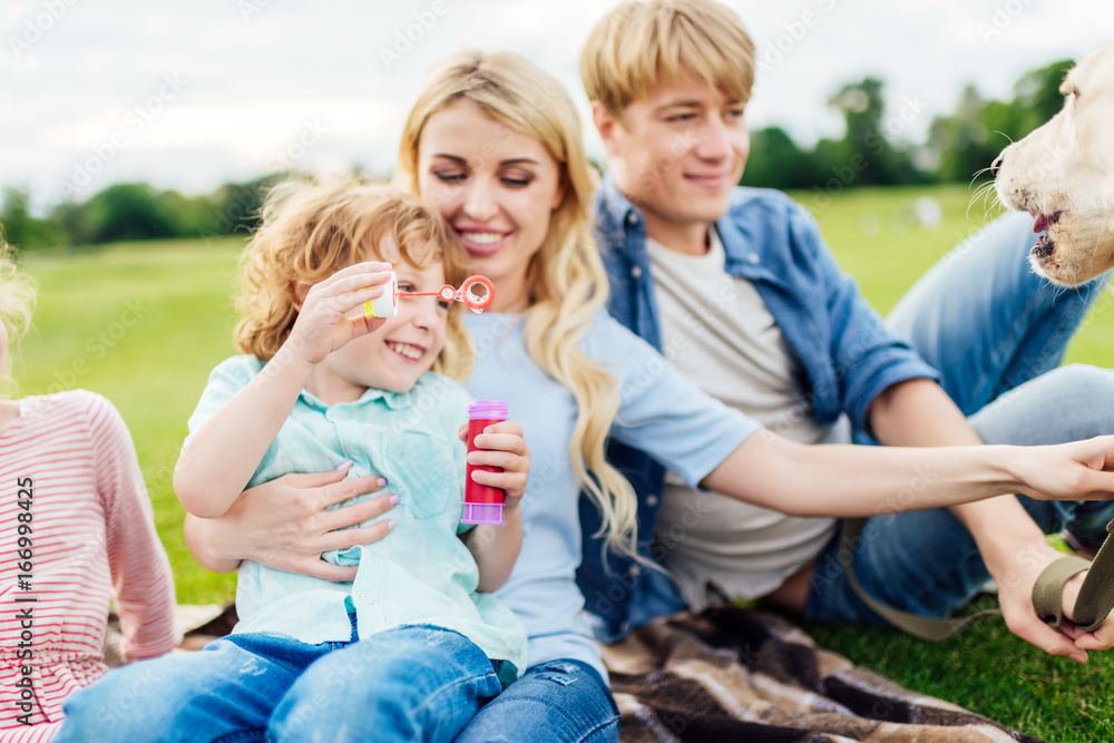 happy young parents with cute little son blowing soap bubbles together in park