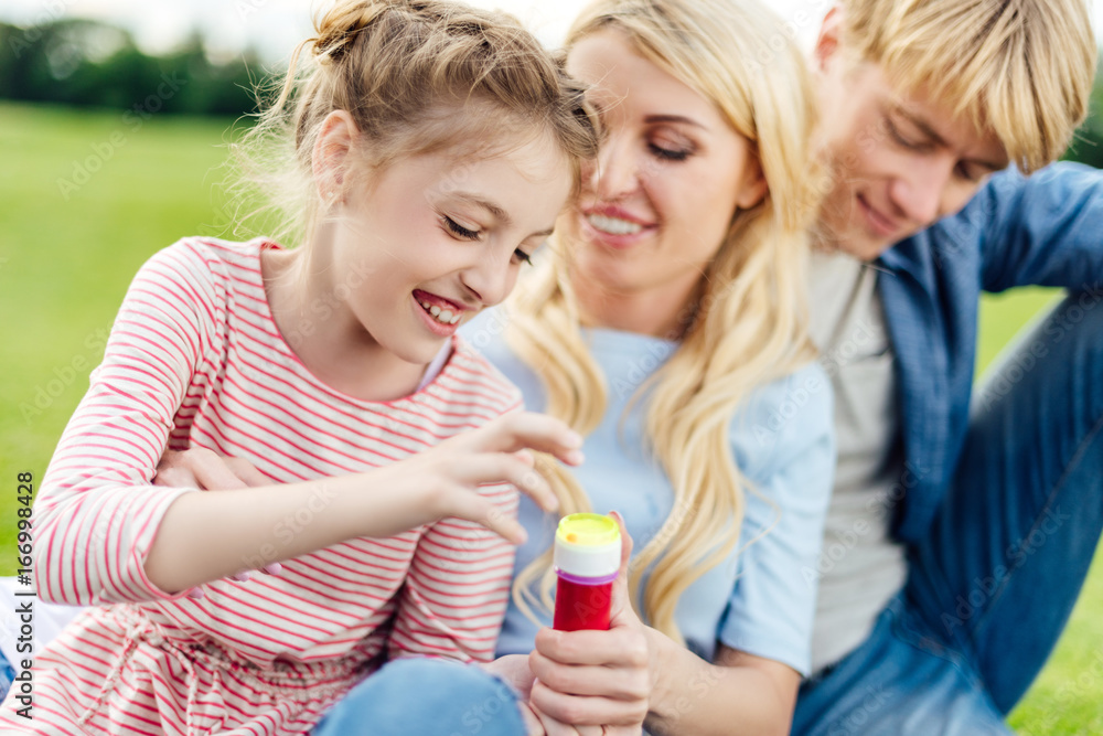 happy young parents with cute smiling daughter blowing soap bubbles together in park happy young parents with cute smiling daughter blowing soap bubbles together in park