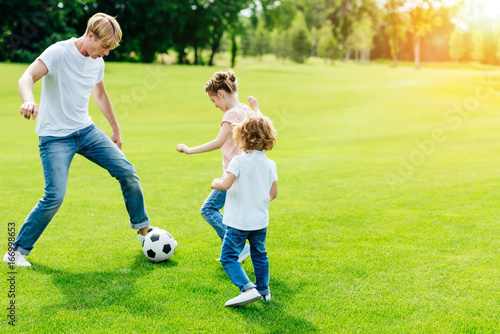 young father with cute little children playing soccer on green grass in park