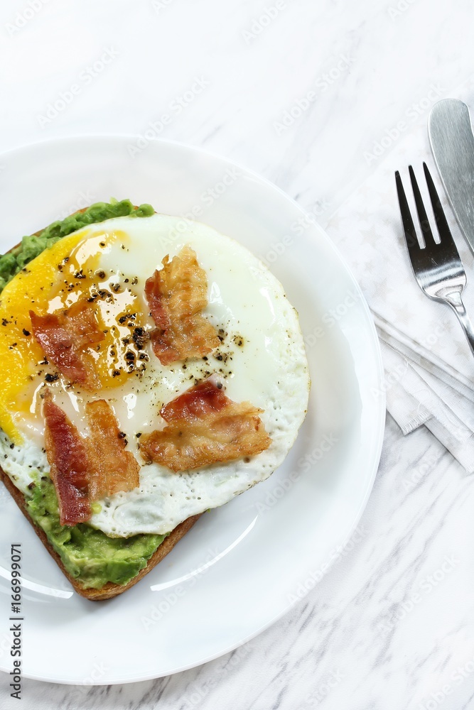 Avocado bread egg toast  topped with bacon and pepper, top down view