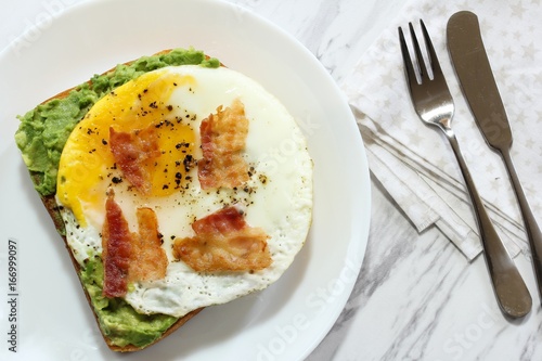 Avocado bread egg toast  topped with bacon and pepper, top down view