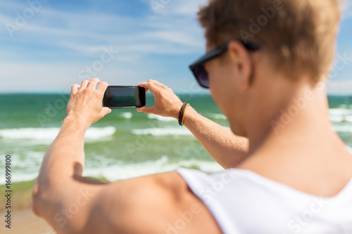 man with smartphone photographing on summer beach