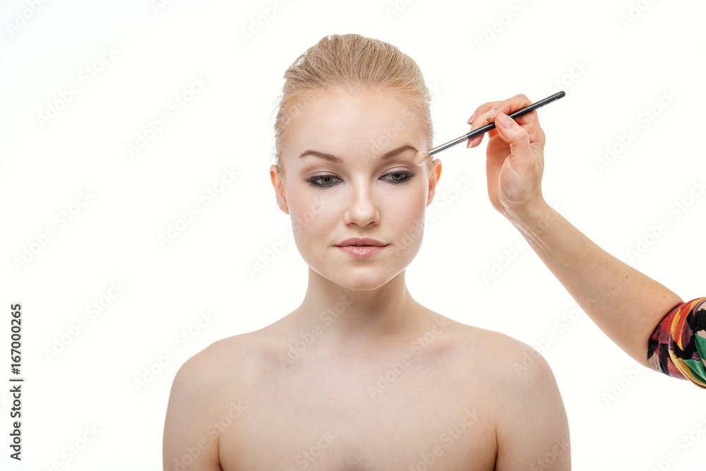 Makeup artist applying eye shadow for beautiful young woman on white background