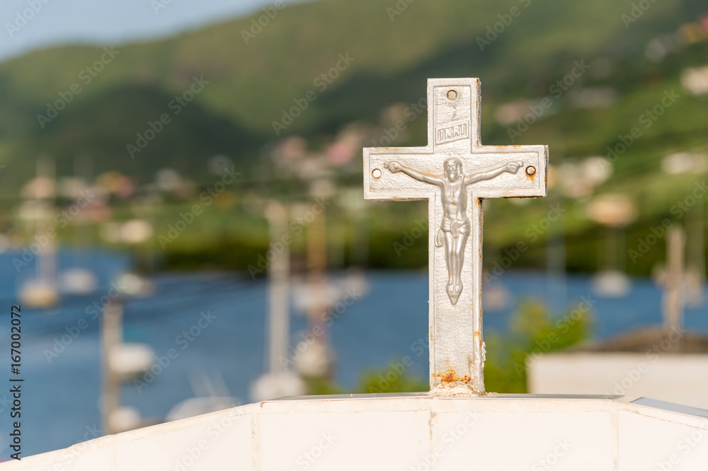 White cross in a cemetery in Martinique with sailboats and sea in background