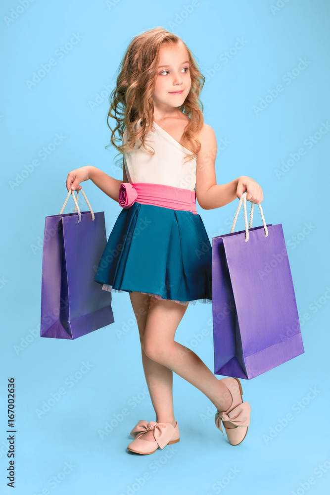 The cute little caucasian brunette girl in dress holding shopping bags