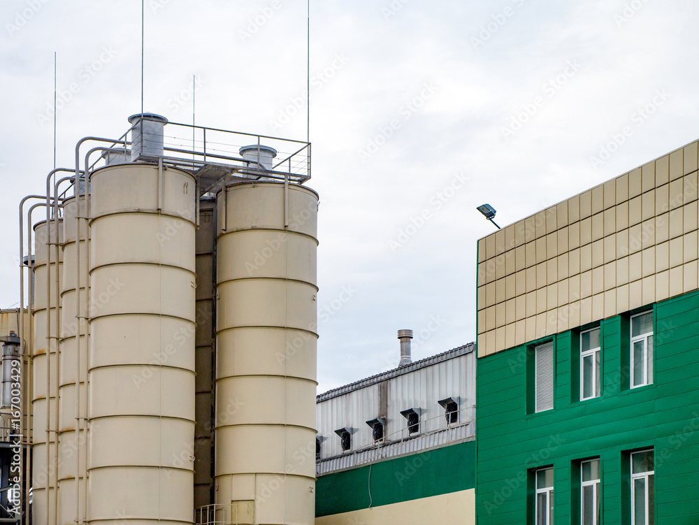  Industrial building external view with tanks, blue sky. Green and white front