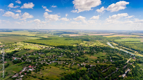 Beautiful view of a typical Ukrainian village surrounded by fields  green forests  small river and blue sky with white clouds. Aerial view.