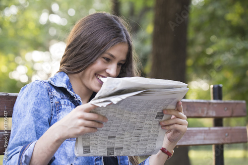 Beautiful young smiling woman, teenager, reading the newspaper in the park