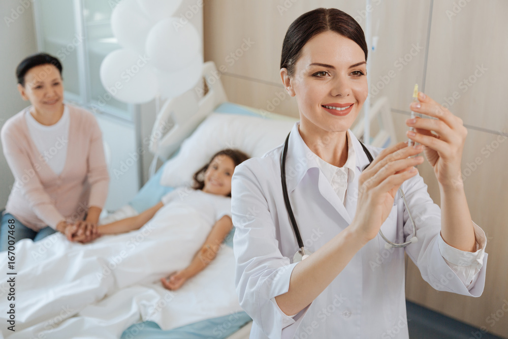 Obraz premium Cheerful positive doctor holding a syringe