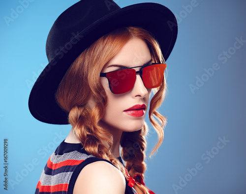Fashion Model Sexy Girl. Hipster woman Cheeky emotion. Stylish Summer Outfit. Redhead woman in Fashion Sunglasses, Glamour Hat. Trendy Black fashion Hat. Playful Summer Hairstyle
