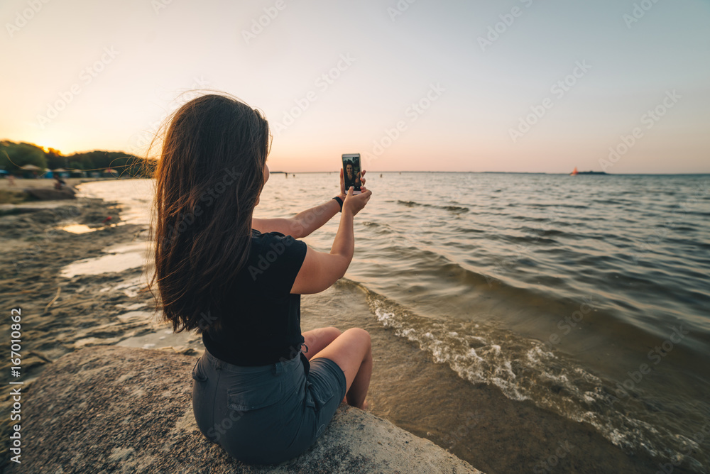 woman sits on a beach and takes picture of the seaside