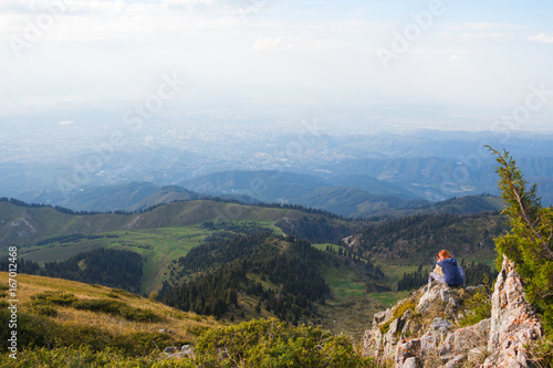 Young woman sitting on top of a mountain. Back view. Tourism concept background.