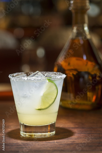 Elegant margarita with slice of lime against warm background with an unlabeled bottle of reposado tequila.