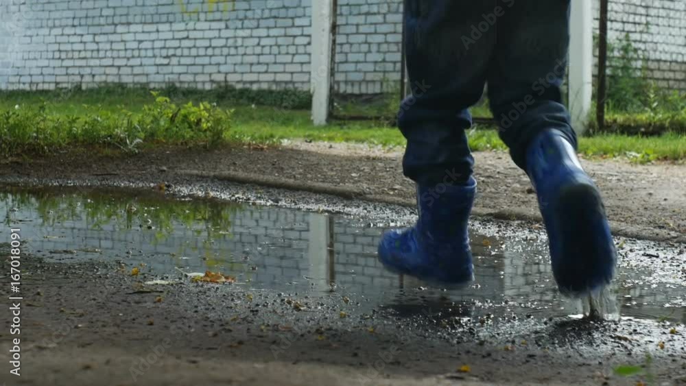 Low angled shot of baby walking and jumping in the pool in the rubber boots Low angled shot of baby walking and jumping in the pool in the rubber boots