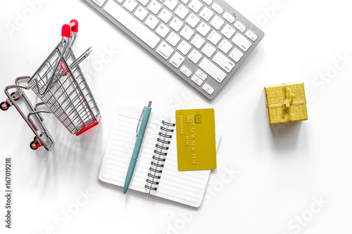 Online shopping concept. Shopping trolley near bank card and keyboard on white background top view