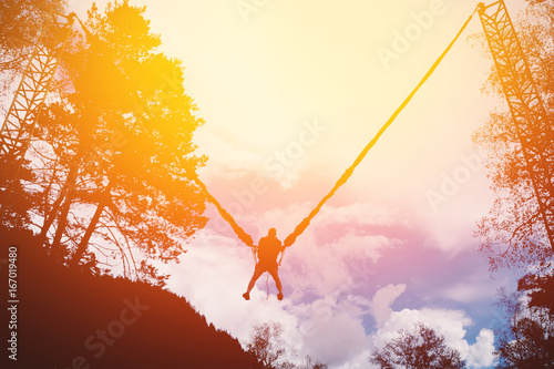 Man jumping on a rope up on a slingshot device. High contrast, silhouette of a man. Shine of the sun.