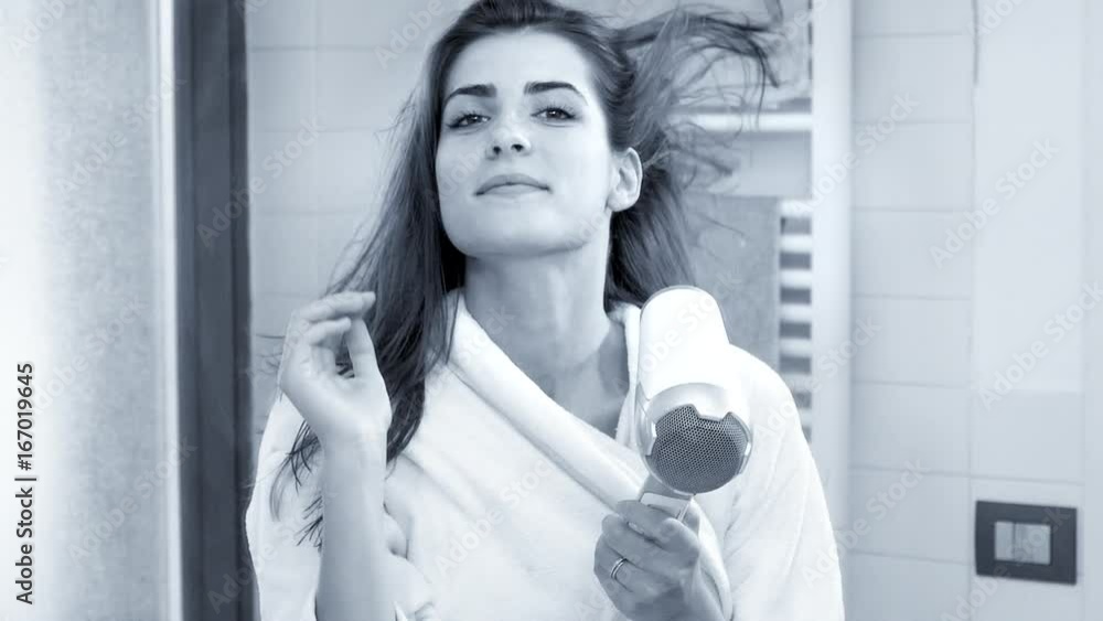 Beautiful woman making long hair fly with blow dryer super slow motion looking camera black and white Beautiful woman making long hair fly with blow dryer super slow motion looking camera black and white