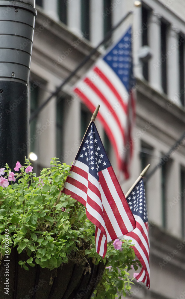 Three USA flags waving in the streets of Manhattan, two in a flower pot stand and one in a building